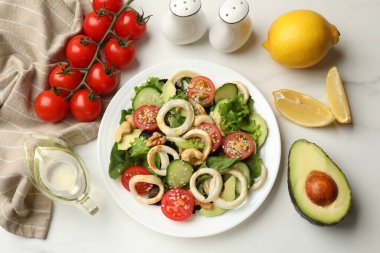 Lezzetli salata, mürekkep balığı halkaları ve beyaz mermer masa üzerindeki malzemeler.