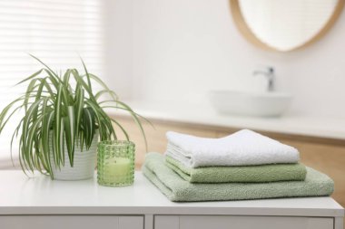 Temiz havlu, mum ve bitki yığını banyodaki beyaz masanın üzerinde. Metin için boşluk