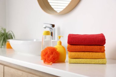 Lavabonun yanındaki tezgahta taze havlu, kozmetik ürünler ve sünger yığını.