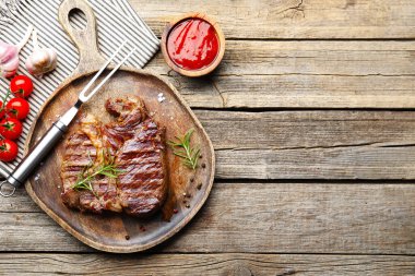 Biberiyeli ızgara biftek, baharat, ketçap, çatal ve ahşap sehpa üzerindeki ürünler. Metin için boşluk