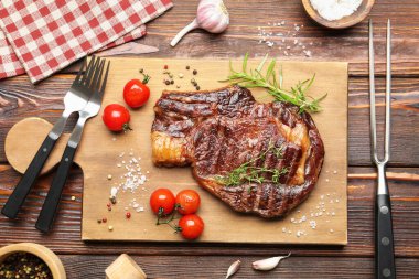 Delicious grilled beef steak with herbs, spices and products on wooden table, flat lay