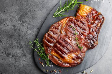Delicious grilled beef steak with herbs and spices on grey textured table, top view. Space for text