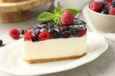 Piece of delicious cheesecake with berries and mint on light grey table, closeup