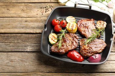 Tavada ızgara biftek, biberiye ve sebzeler ahşap masada, üst tarafta. Metin için boşluk