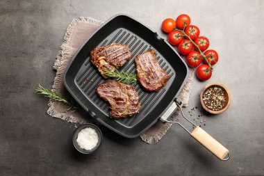 Izgara biftekli tava, biberiye, domates ve baharatlar gri desenli masa, düz uzanma
