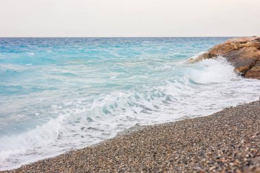 Dalgalı deniz manzarası ve kumsaldaki çakıl taşları.