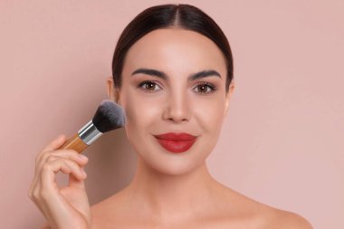 Güzel bir kadın pembe arkaplanda fırçayla makyaj yapıyor.