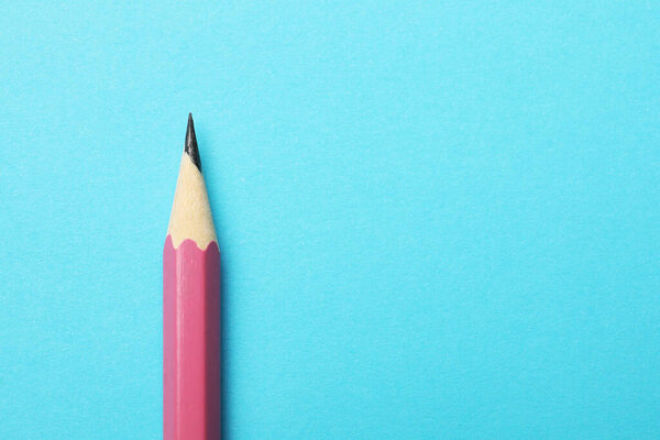 One sharp graphite pencil on light blue background, top view. Space for text