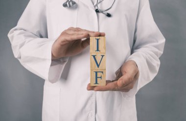 Tüp bebek tedavisinde. Doktor, gri arka plana karşı tüp bebek kısaltmalı tahta küpleri tutuyor. Yakın plan.