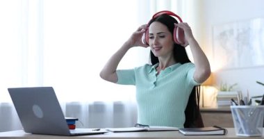 Kulaklıklı bir kadın bilgisayarla kapalı bir masada çevrimiçi sınavdan geçiyor.