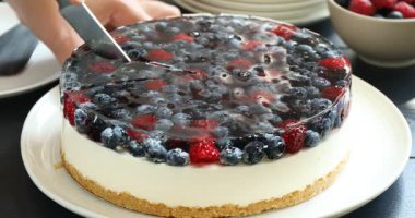 Lezzetli peynirli keki böğürtlenli kesen ve siyah ahşap masada bir parça tatlı yiyen kadın.