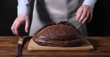 Ahşap masada taze ekmek doğrayan fırıncı, yakın plan.