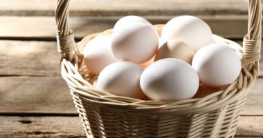 Hasır sepetteki çiğ tavuk yumurtaları ahşap masada, yakın plan. Kamera sola hareket ediyor