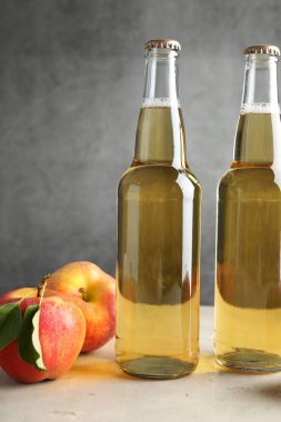 Cam şişelerdeki lezzetli elma şarabı ve elmalar gri arka planda, yakın plan