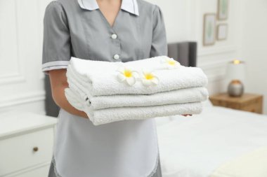 Otel odasında beyaz havlu yığınıyla oda hizmetçisi ve tesisat çiçekleri, yakın plan.