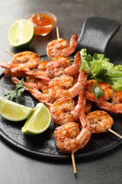 Lezzetli ızgara karidesli şişler, limon dilimleri, maydanoz, marul ve sos gri masada, yakın plan. Lezzetli deniz ürünleri yemeği.