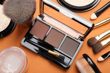 Göz farı paleti, kaş jölesi ve turuncu arka planda makyaj fırçaları, düz yatıyordu.