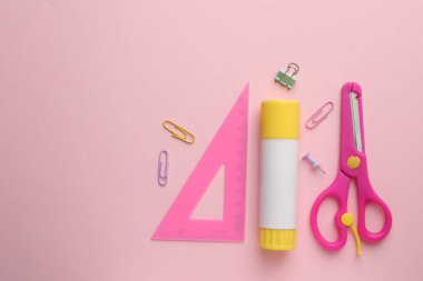 Yapıştırıcı, cetvel, makas ve ataçlar pembe arka planda, düz konum. Metin için boşluk