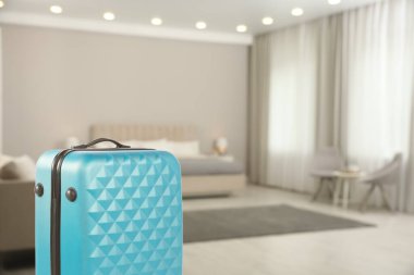 Spacious hotel room with comfortable furniture and guest suitcase, selective focus