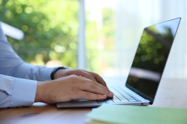 İçerideki ahşap masada dizüstü bilgisayarda çalışan adam, yakın plan.