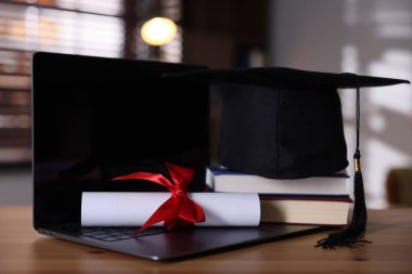 Mezuniyet şapkası, dizüstü bilgisayar, kitaplar ve diploma ahşap masada, yakın plan.