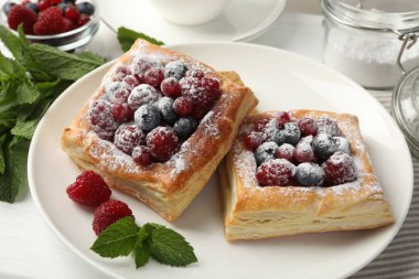 Böğürtlenli, pudra şekerli ve naneli börekler beyaz masada, yakın plan.