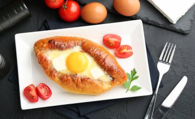 Peynir ve yumurtalı leziz khachapuri siyah desenli masada servis edilir.