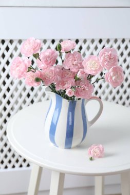 Beautiful carnation flowers in jug on white table indoors