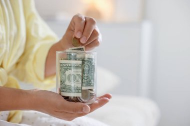 Kadın evin içinde kavanoza para koyuyor, yakın plan. Metin için boşluk