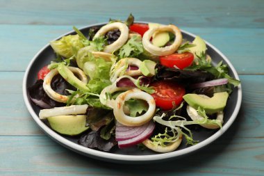 Kalamar halkalı lezzetli salata, avokado ve sebzeler açık mavi ahşap masada, yakın plan.