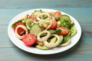 Kalamar halkalı lezzetli salata, avokado, fındık ve sebzeler açık mavi ahşap masada, yakın plan.