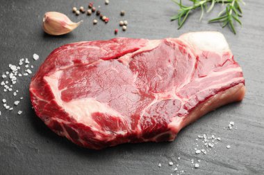 Bir parça çiğ et ve baharat siyah masada, yakın plan.