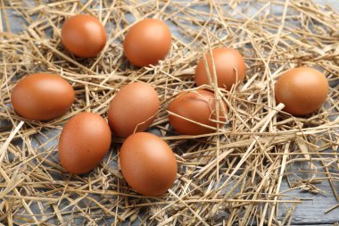 Raw chicken eggs and straw on grey wooden table, closeup