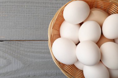 Raw chicken eggs in wicker basket on grey wooden table, top view. Space for text