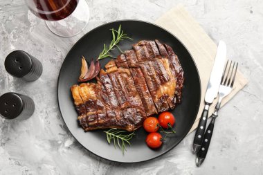 Biberiye, soğan ve domatesli leziz ızgara biftek. Gri desenli masada servis ediliyor.