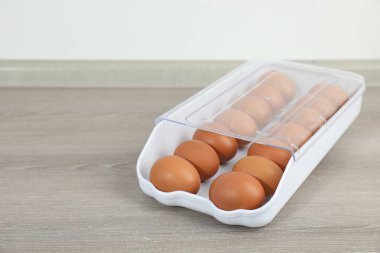 Ahşap tezgahta plastik kabın içinde çiğ tavuk yumurtası, yakın plan. Metin için boşluk