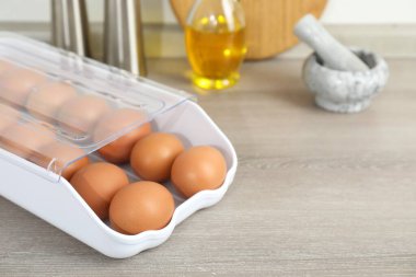 Plastik kabın içinde çiğ tavuk yumurtası ve ahşap tezgahın üzerinde mutfak aletleri, yakın plan.