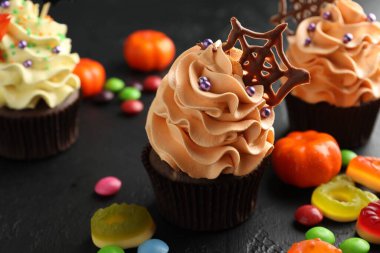 Çikolata ağlı lezzetli kekler ve koyu dokulu masa üzerinde renkli şekerler, yakın plan. Cadılar Bayramı