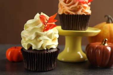 Kırmızı yapraklı lezzetli kapkekler ve gri desenli balkabakları kahverengi arka planda, yakın plan. Sonbahar atmosferi