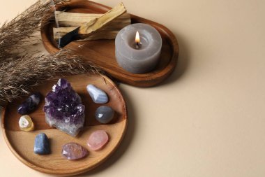 Farklı güzel değerli taşlar, kurumuş sazlıklar, palo santo çubukları ve bej arka planda yanan mumlar. Metin için boşluk
