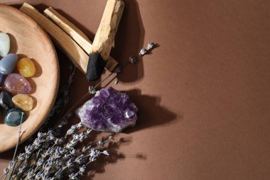 Farklı güzel değerli taşlar, palo santo çubukları ve kahverengi arka planda lavanta çiçekleri. Metin için boşluk