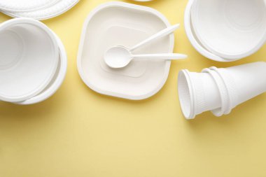 Tek kullanımlık plastik sofra takımı soluk sarı arka planda, düz yerde. Metin için boşluk