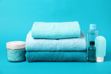 Açık mavi arka planda taze havlu ve kozmetik ürünleri yığını
