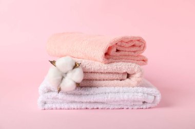 Pembe arka planda bir yığın taze havlu ve pamuk çiçeği.