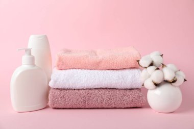 Pembe arka planda taze havlu, kozmetik ürünler ve pamuk çiçekleri yığını