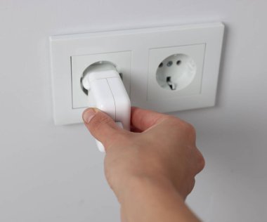 USB adaptörünü beyaz duvardaki güç soketine takan adam, kapat