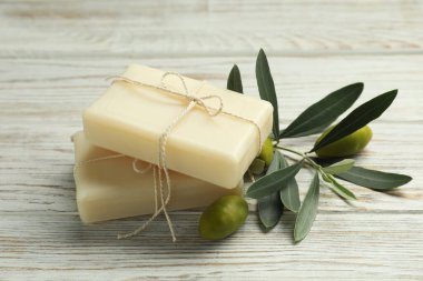 Natural soap bars with olives and green leaves on white wooden table, closeup