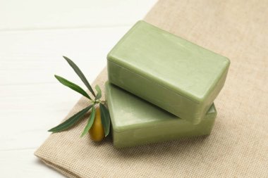 Natural soap bars with olive and green leaves on white wooden table, closeup