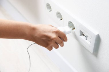 USB adaptörünü kabloyla beyaz duvardaki güç prizine bağlayan kadın, kapat