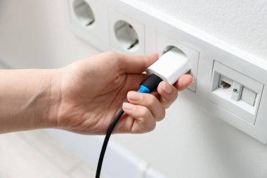 USB adaptörünü kabloyla beyaz duvardaki elektrik prizine takan kadın, kapat